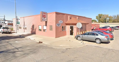 A pink building on a corner with a sign for "East Side" and parked cars nearby.