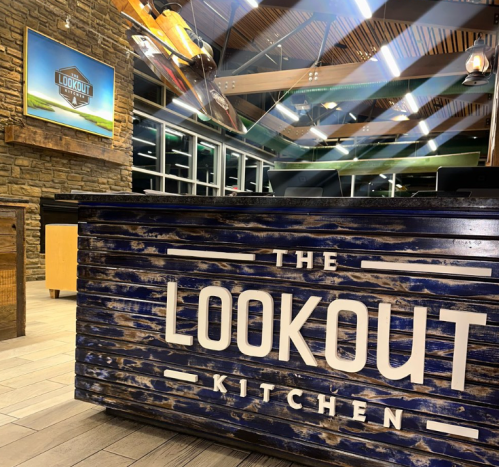 Interior of The Lookout Kitchen, featuring a wooden reception desk and a scenic wall display. Warm lighting and modern design.