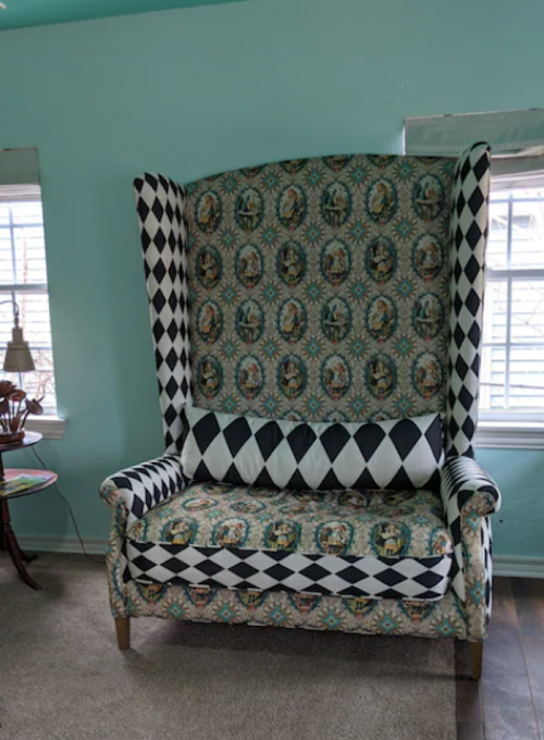 A large, patterned wingback chair with a mix of floral and geometric designs in a light blue room.