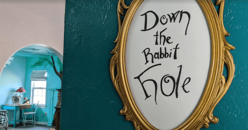 A decorative mirror with the text "Down the Rabbit Hole" on a vibrant teal wall, with a glimpse of a cozy room in the background.