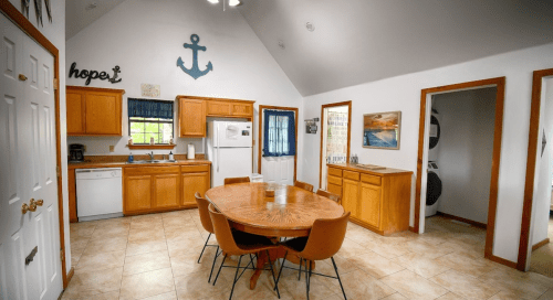 Bright kitchen with wooden cabinets, a round dining table, and nautical decor, featuring an anchor and the word "hope."