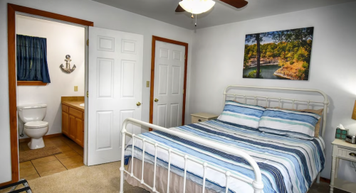 Cozy bedroom with a striped bedspread, a bathroom door, and a nature-themed wall art.