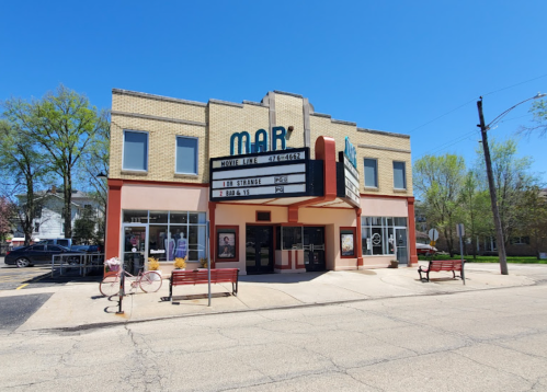 A vintage movie theater with a marquee displaying "Doctor Strange," surrounded by trees and benches.