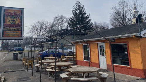 A colorful restaurant exterior with outdoor seating and a large sign, set in a quiet area with trees in the background.