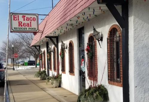 Exterior of El Taco Real restaurant, featuring festive decorations and a sign for Mexican food. Snow on the ground.