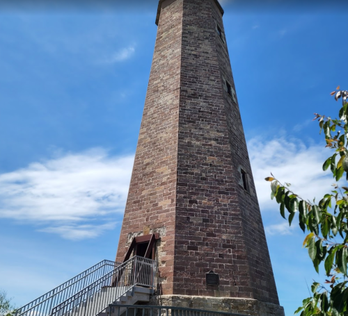 A tall stone tower with a staircase leading up, set against a blue sky with scattered clouds.