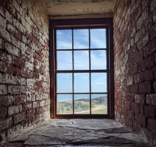 A rustic brick window frame with a view of a blue sky and landscape outside.