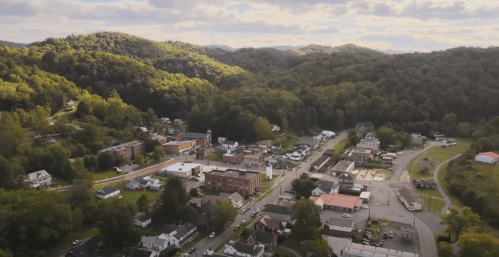 Aerial view of a small town surrounded by lush green mountains under a partly cloudy sky.