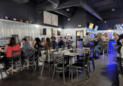 A lively restaurant interior with patrons dining and socializing at tables and the bar, featuring a modern decor.