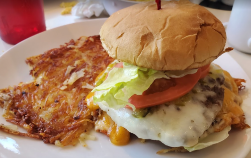 A cheeseburger with lettuce, tomato, and melted cheese, served with crispy hash browns on a white plate.