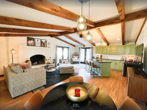 Cozy living space with exposed beams, a fireplace, and a kitchen featuring green cabinets and modern decor.