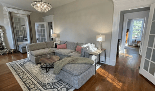 Cozy living room with a gray sectional sofa, a coffee table, and a chandelier, featuring warm natural light.