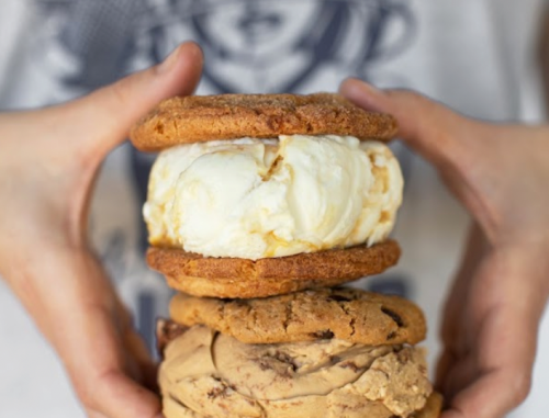 A person holds three stacked cookie sandwiches filled with ice cream, showcasing a delicious dessert treat.