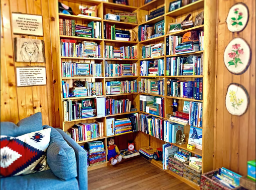 Cozy corner of a room featuring a wooden bookshelf filled with books, a blue couch, and decorative items.