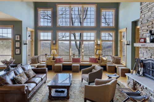 Spacious living room with large windows, mountain views, leather sofa, and cozy seating by a stone fireplace.