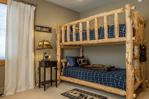 Cozy bedroom featuring a wooden bunk bed, plaid bedding, a nightstand, and a decorative lamp.