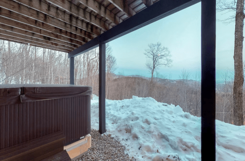 A hot tub on a deck overlooking a snowy landscape and distant mountains under a clear sky.