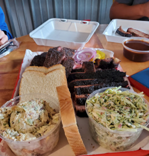 A platter of barbecue brisket, sliced bread, coleslaw, and potato salad on a red tray.