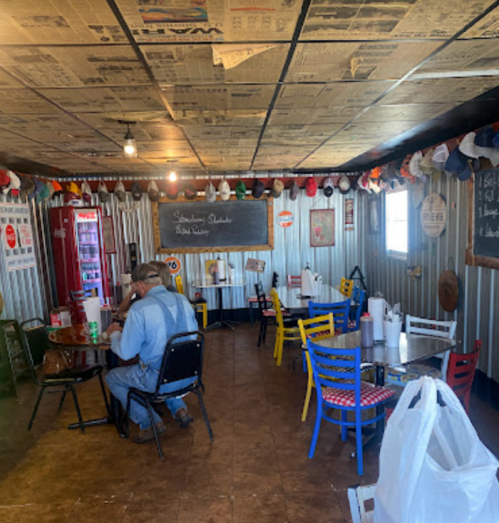 A cozy diner with newspaper-covered ceiling, colorful chairs, and a man eating at a table.