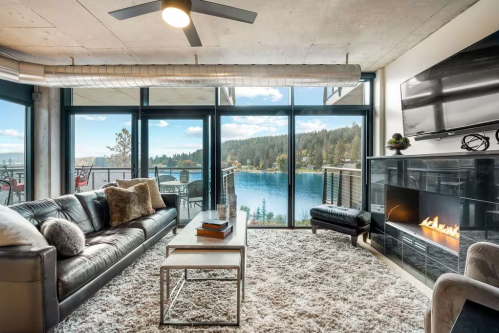 Modern living room with a lake view, featuring a leather sofa, coffee table, and a cozy fireplace.