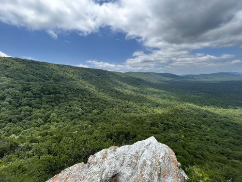 A panoramic view of lush green mountains under a partly cloudy sky, with a rocky foreground.