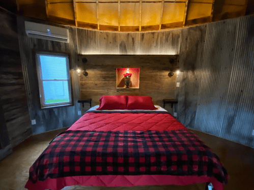 Cozy bedroom with a round design, featuring a red and black plaid blanket, wooden walls, and soft lighting.
