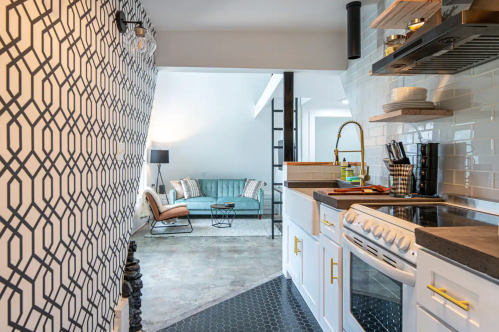 Modern kitchen with geometric wallpaper, sleek appliances, and a view of a cozy living area with a blue sofa.