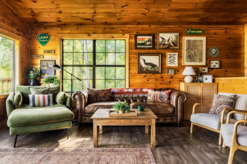 Cozy wooden cabin living room with a green chair, leather sofa, wooden table, and nature-themed decor.