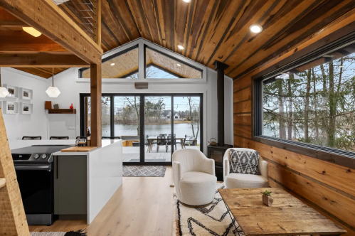 Cozy interior of a modern cabin with wooden beams, large windows, and a view of a lake. Stylish furniture and decor.