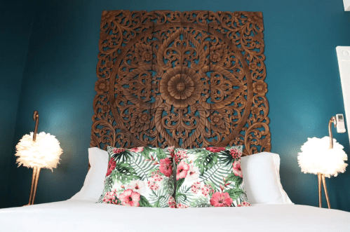 A cozy bedroom featuring a large wooden wall art, floral pillows, and stylish lamps on either side of the bed.