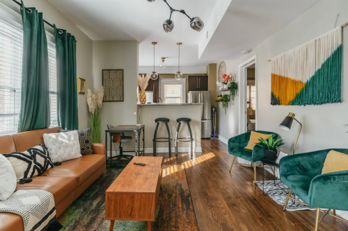Cozy living room with a brown sofa, green chairs, wooden coffee table, and modern decor, featuring natural light and plants.