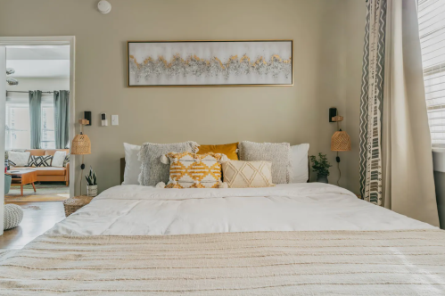 Cozy bedroom with a large bed, decorative pillows, and a wall art piece, featuring warm tones and natural textures.