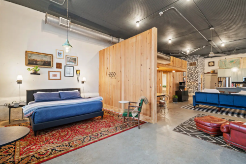 A stylish, open-concept living space featuring a bed, wooden partition, and modern decor with a cozy rug.