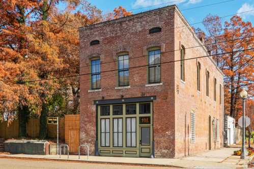 Historic brick building with large windows, surrounded by autumn trees and a clear blue sky.