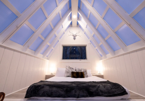 Cozy bedroom with a sloped ceiling, large windows, and a bed adorned with pillows and a soft blanket.