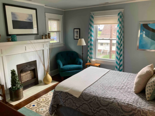 Cozy bedroom with a bed, teal armchair, fireplace, and large window with chevron curtains.