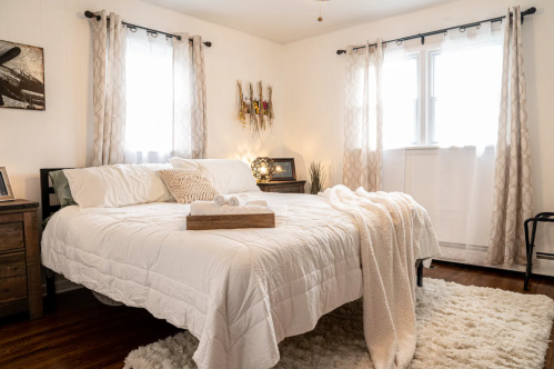 Cozy bedroom with a large bed, soft blankets, and natural light from windows, featuring a warm, inviting decor.