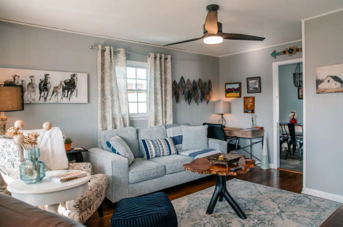 Cozy living room with a gray sofa, decorative art, a wooden coffee table, and a dining area in the background.