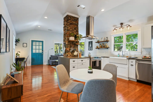 Bright, modern kitchen and dining area with a stone column, wooden floors, and large windows letting in natural light.