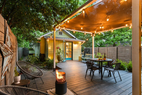 Cozy outdoor patio with string lights, a fire pit, and a charming yellow house in the background.