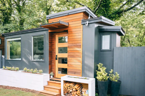 A modern tiny house with wooden accents, a stylish front door, and a small garden area.