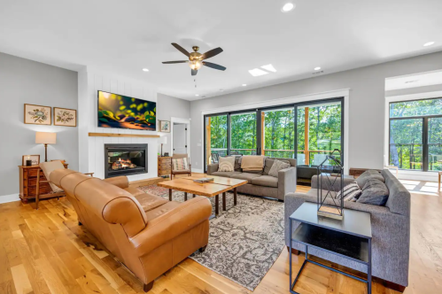 Spacious living room with a fireplace, large windows, comfortable seating, and a wooden coffee table.