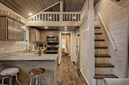 Cozy kitchen and living area with wooden accents, stairs leading to a loft, and modern appliances.