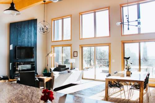 Bright, modern living room with large windows, a cozy sofa, dining table, and a view of the outdoors.