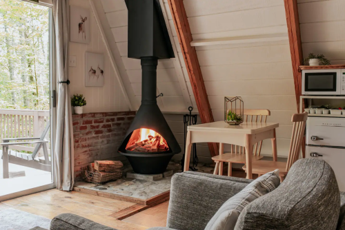 Cozy interior of a cabin featuring a modern fireplace, dining table, and large windows with a view of nature.