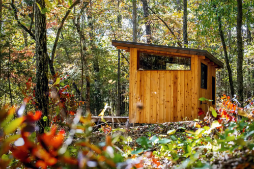 A small wooden cabin nestled among colorful autumn trees in a serene forest setting.