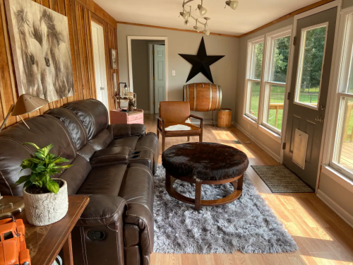Cozy sunroom with leather couch, wooden accents, a star decoration, and a round fur ottoman on a plush rug.
