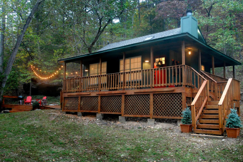 A cozy wooden cabin with a porch, surrounded by trees and outdoor lights, set in a serene natural landscape.