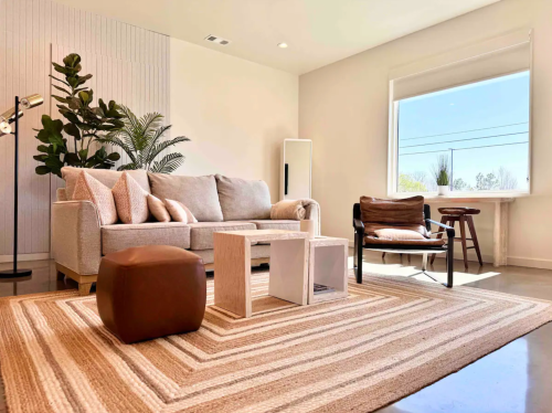 Cozy living room with a light sofa, wooden coffee table, and plants, featuring a large window and modern decor.