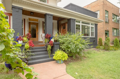 A charming house with a black and white exterior, featuring a welcoming porch and colorful plants along the steps.